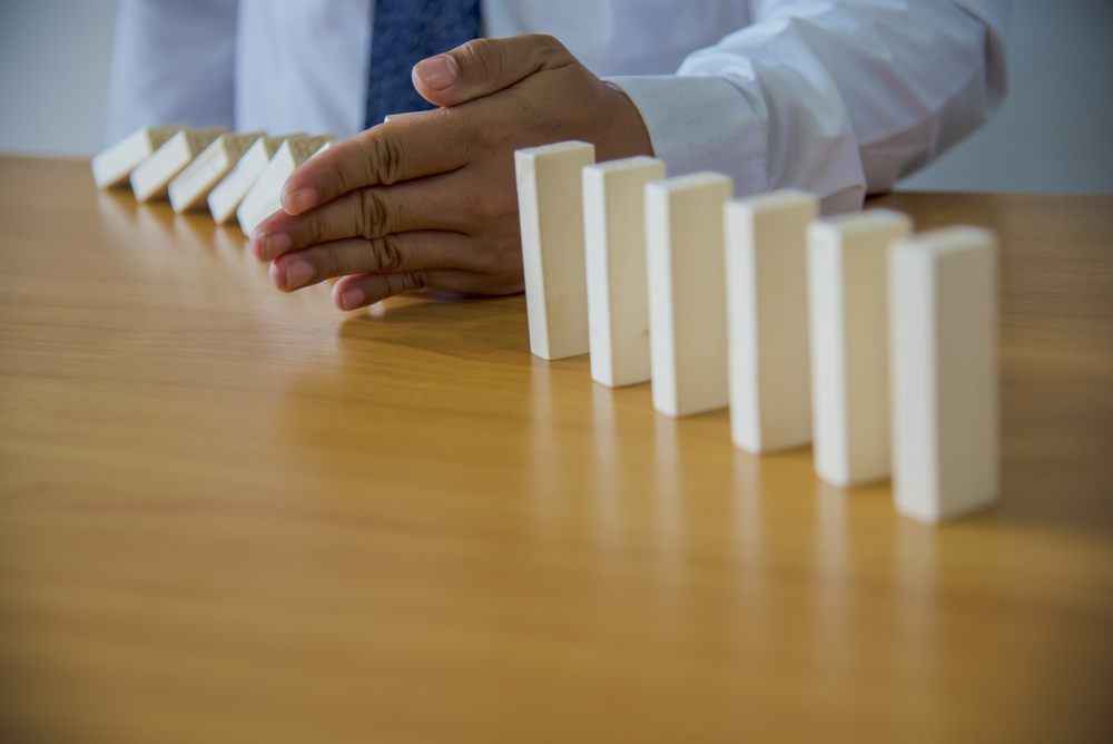 Businesswoman,Hand,Stopping,Dominoes,From,Falling,On,Office,Desk.,Risk