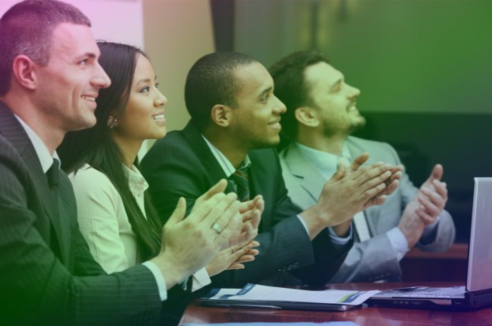 A group of diverse business people sat at a table clapping for the recertification of the ISO 22301 certification for business continuity.